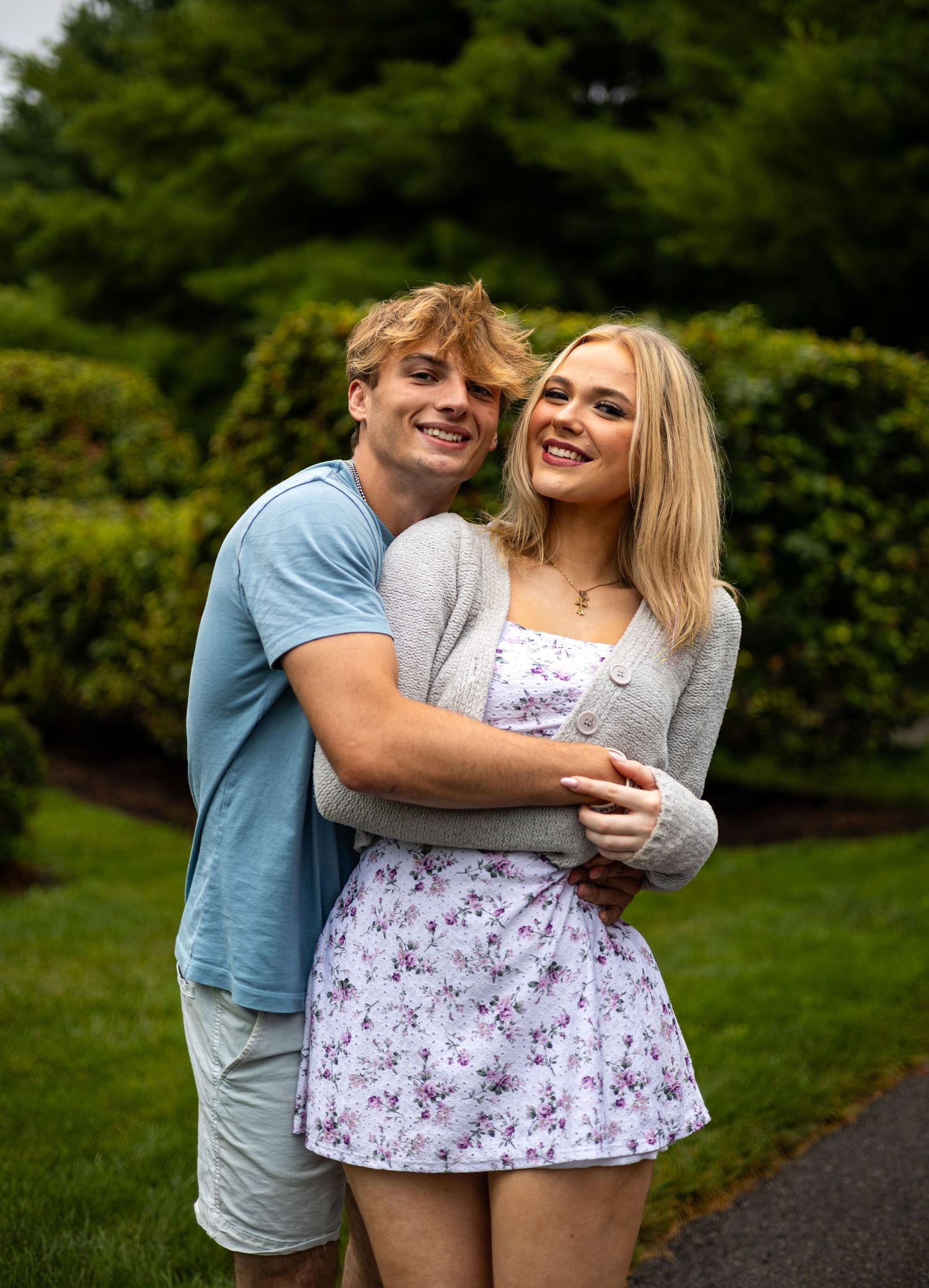 Smiling young couple posing together in a garden, man embracing woman from behind.