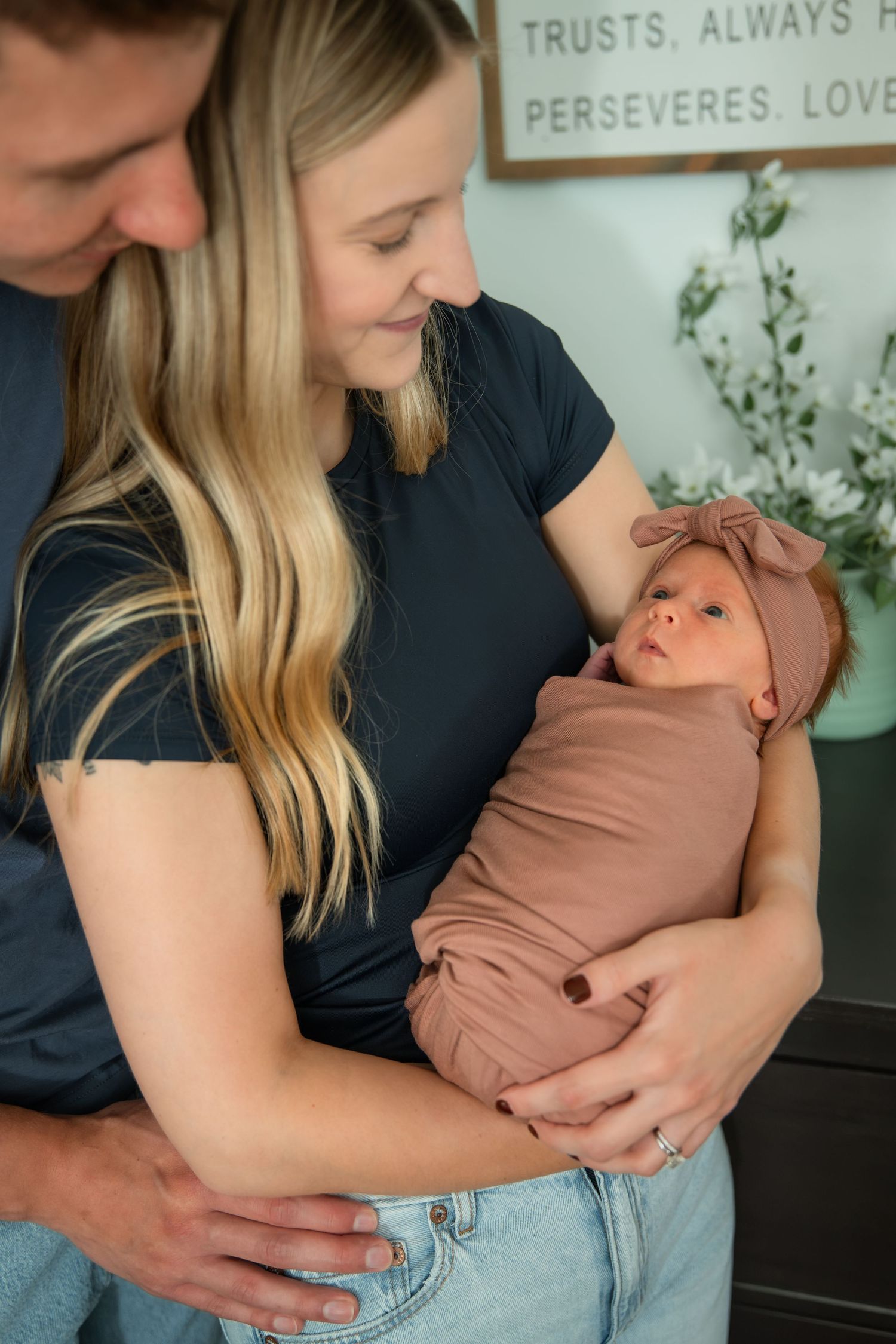 Parents lovingly cradling their swaddled newborn baby in a cozy nursery setting.