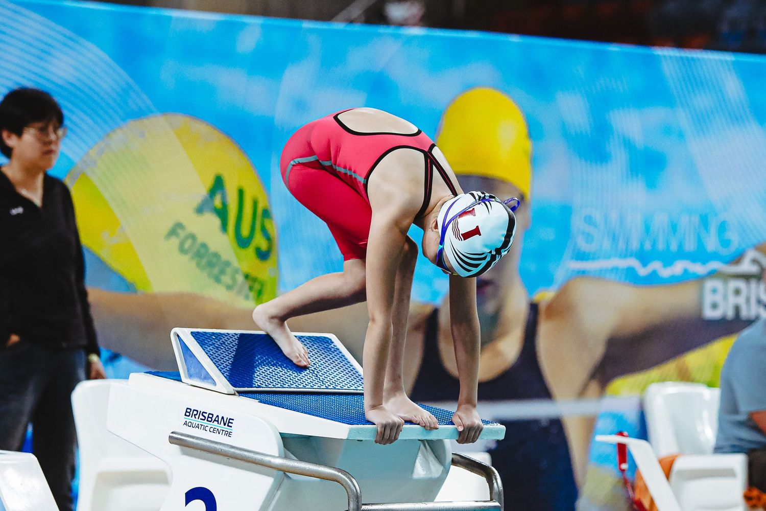 Swimmers prepare on starting blocks at an indoor swimming competition, with lane markers numbered 4 and 5 visible.