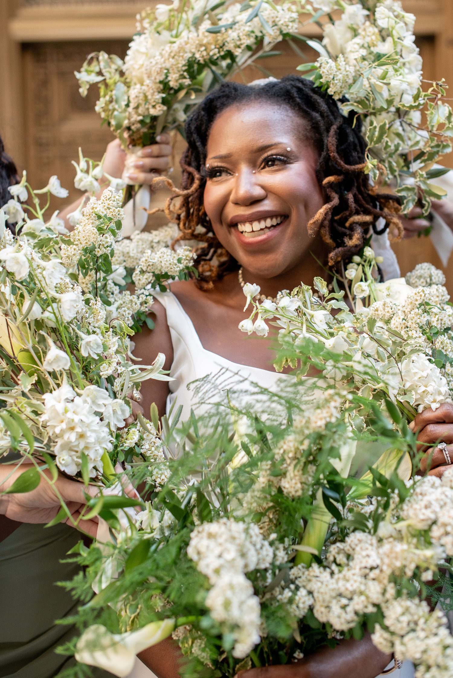 Smiling bride surrounded by lush white floral bouquets on her wedding day.