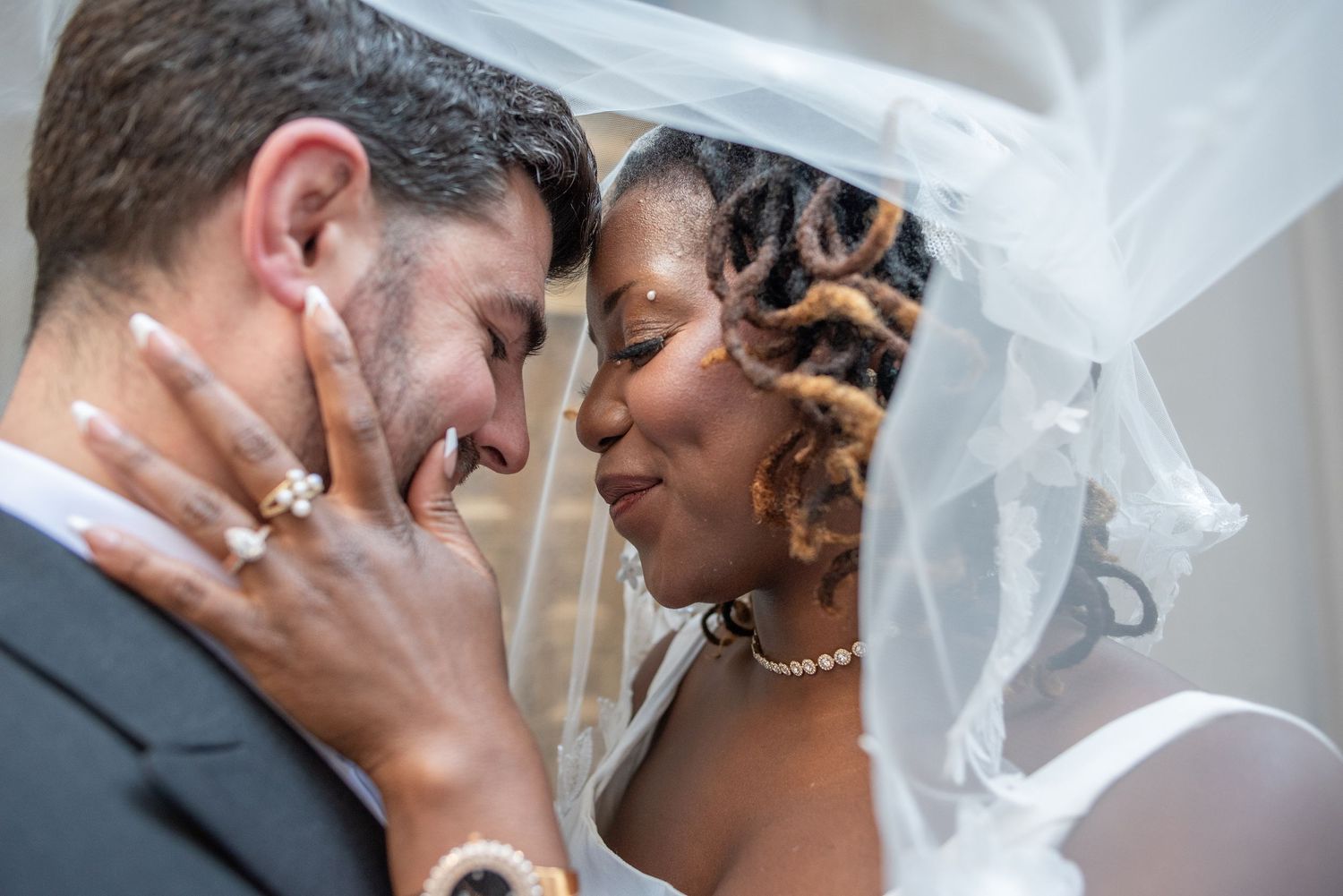 Interracial bride and groom sharing an intimate romantic moment under a flowing white wedding veil.