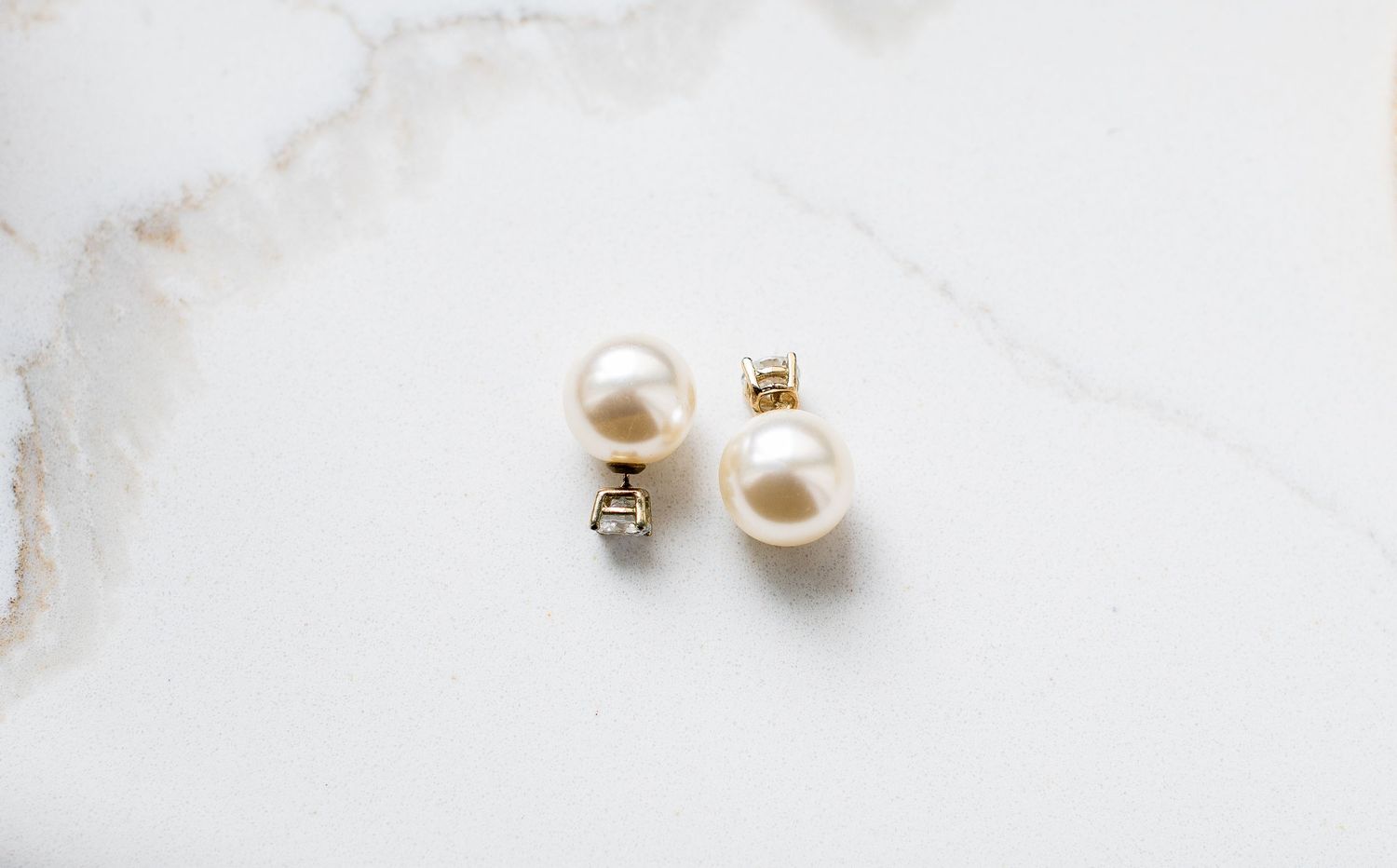 Elegant pearl stud earrings with gold backs displayed on white marble surface.