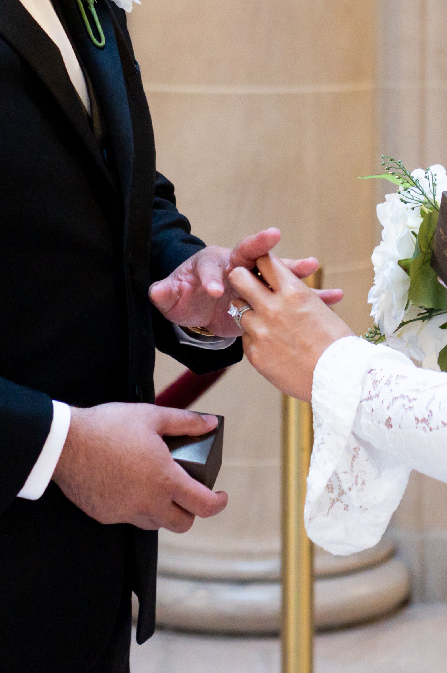 Bride placing wedding ring on groom's finger during ceremony, holding bouquet of white flowers.