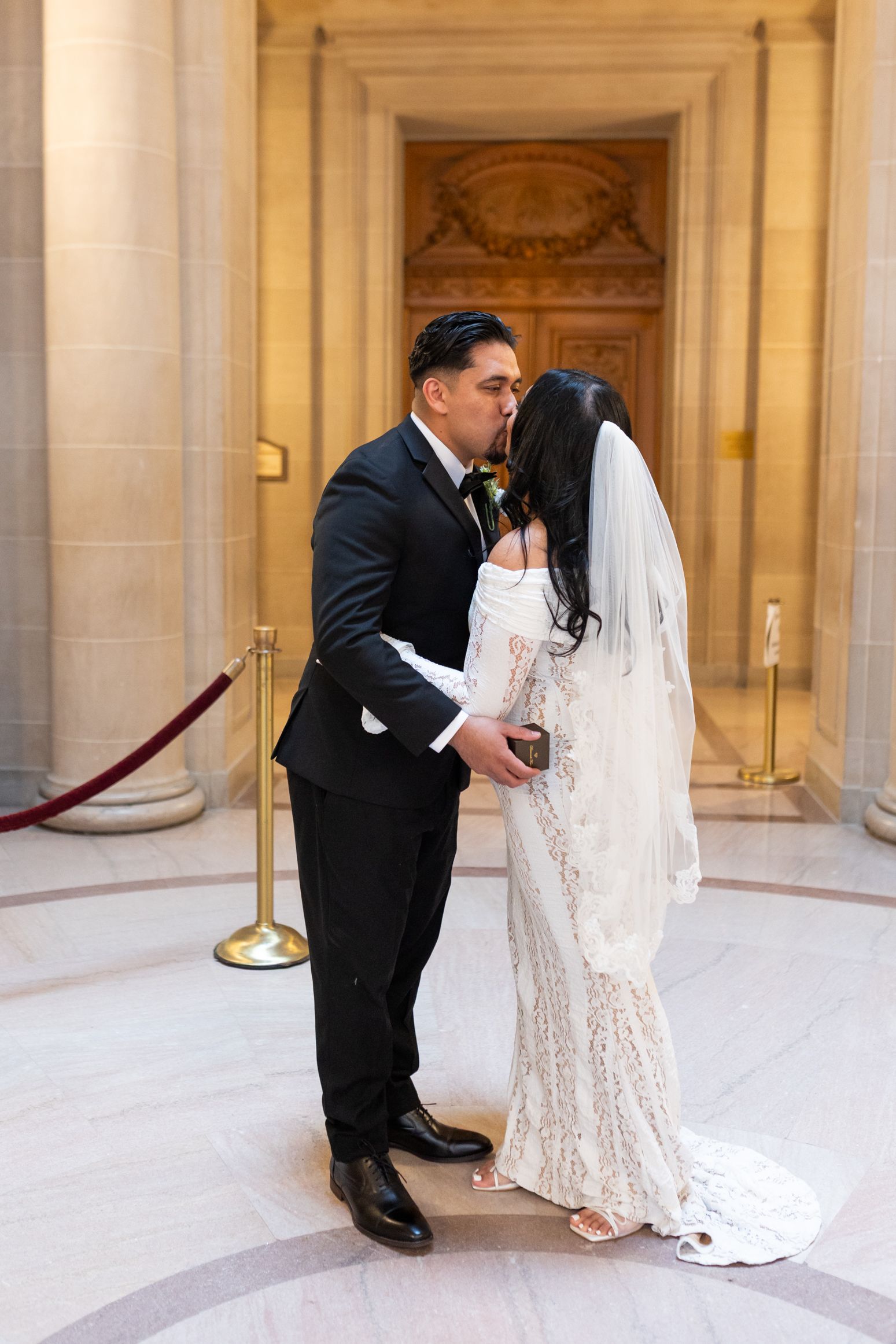 Bride and groom share a romantic kiss at San Francisco City Hall, bride wearing lace gown and veil.