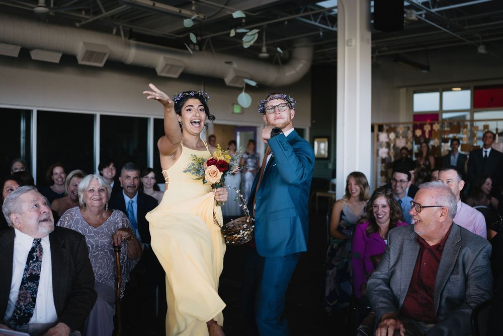 Joyful bride in yellow gown and groom in teal suit celebrate at wedding reception with guests applauding.
