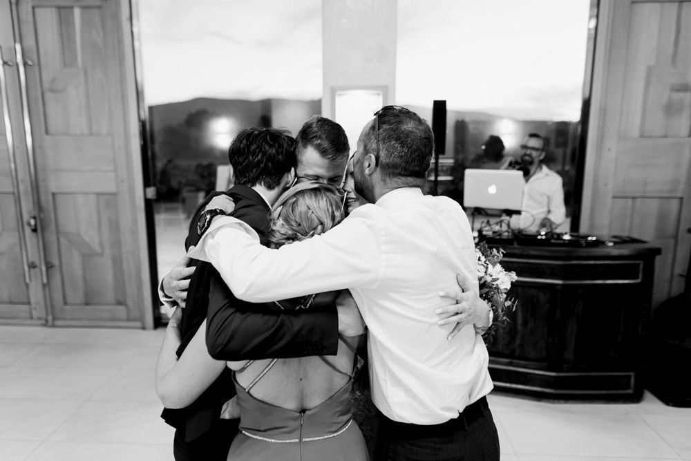 Black and white photo of three people sharing a warm group hug at a wedding reception.