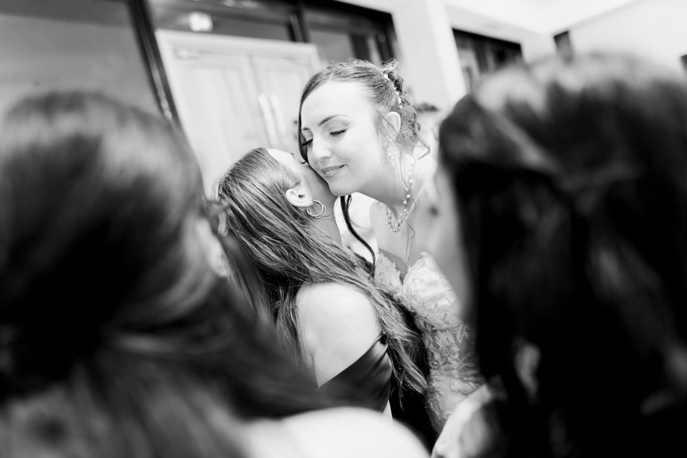 Black and white photo of two women sharing a tender embrace at a social gathering or celebration.