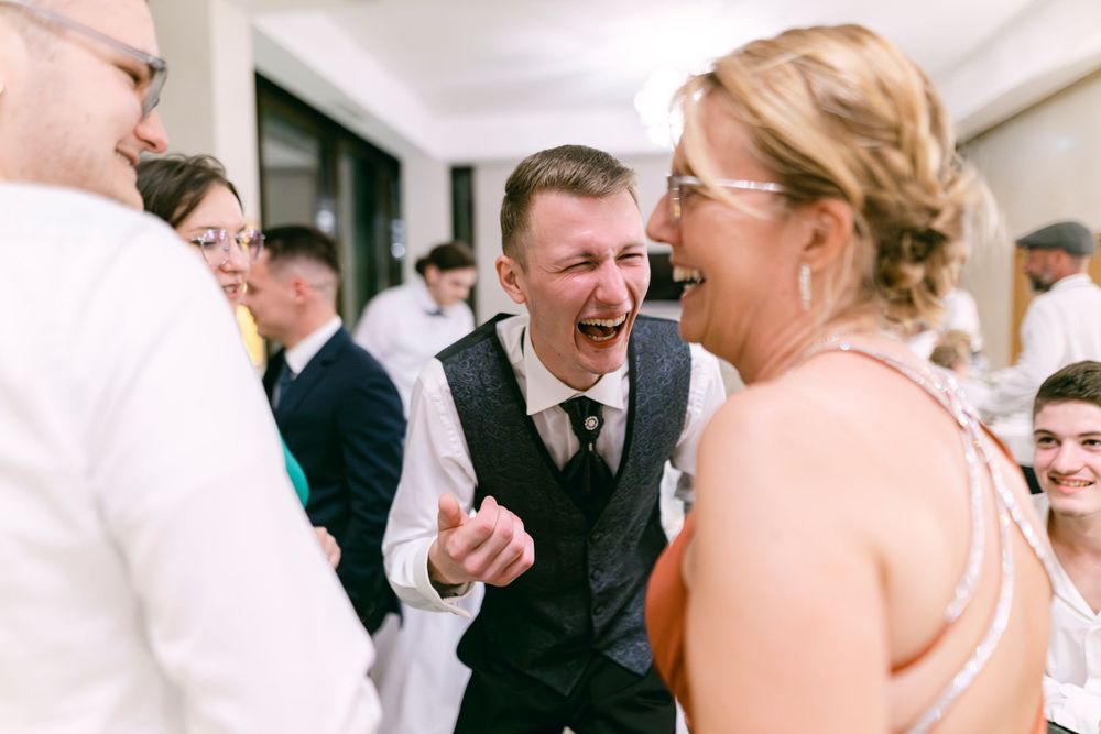 Joyful wedding guests laughing and celebrating together at a reception, with groom in vest sharing a fun moment.
