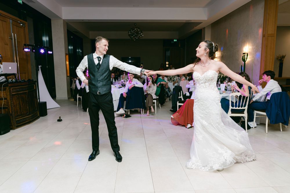 Bride and groom sharing their first dance at an elegant wedding reception venue with guests seated in background.