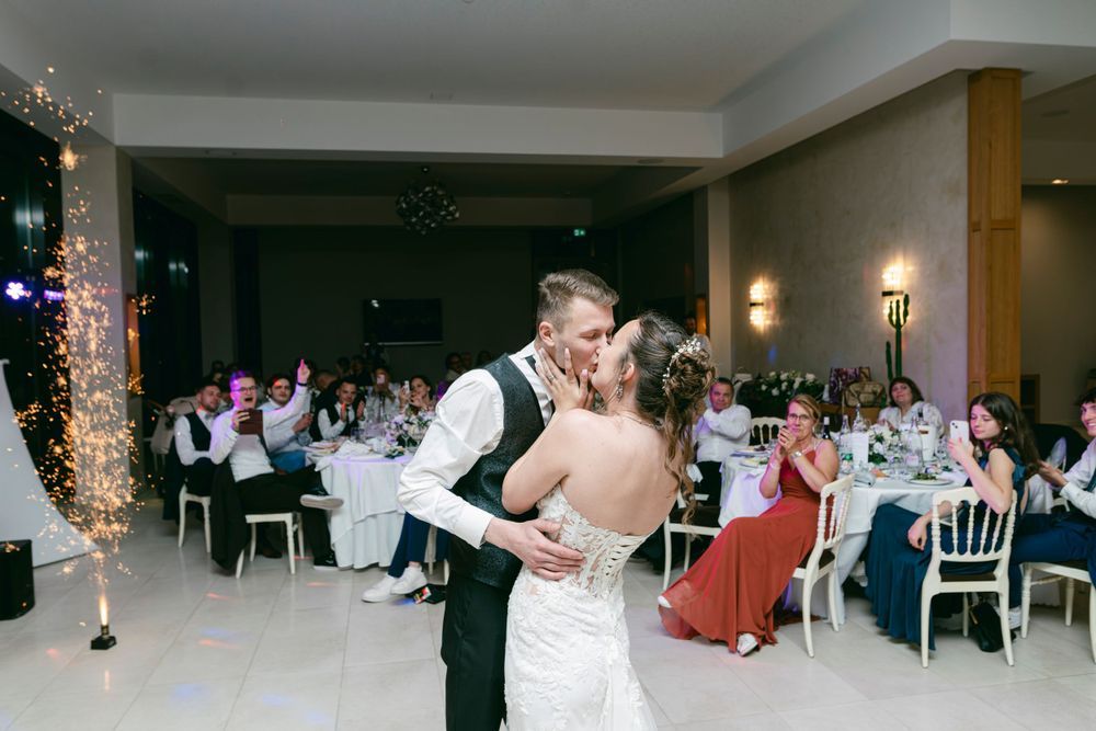 Bride and groom share first dance kiss at wedding reception with sparklers and seated guests in elegant venue.