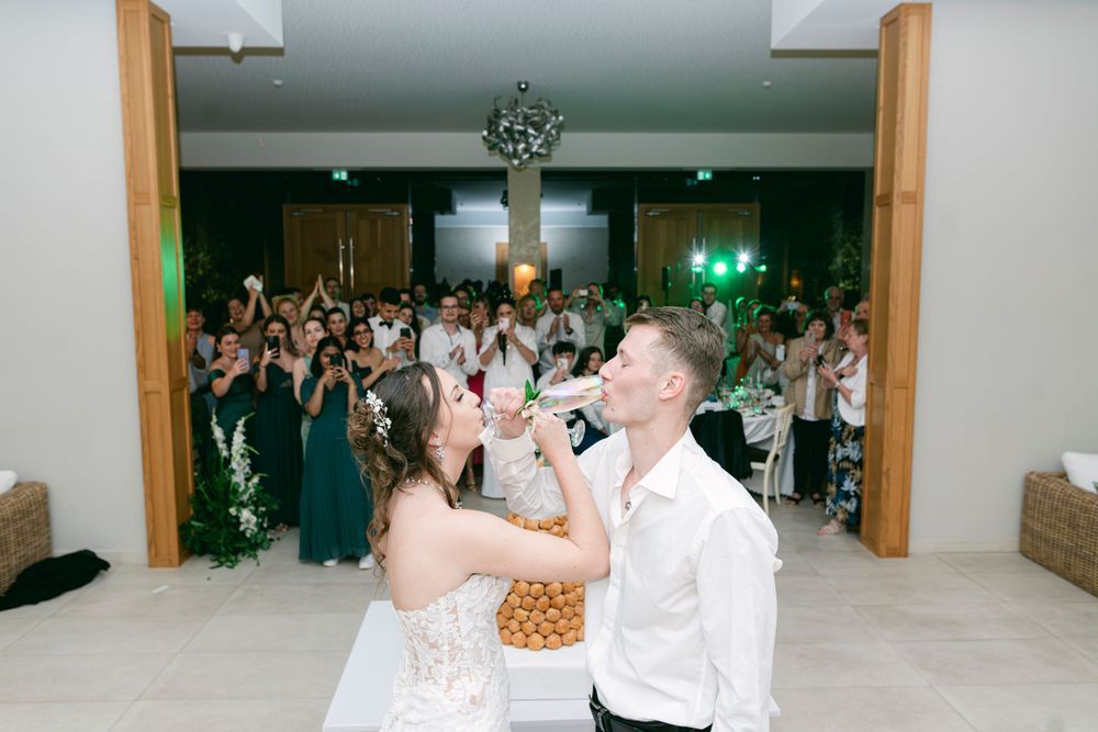 Bride and groom drinking from bottles at wedding reception with guests celebrating in background.