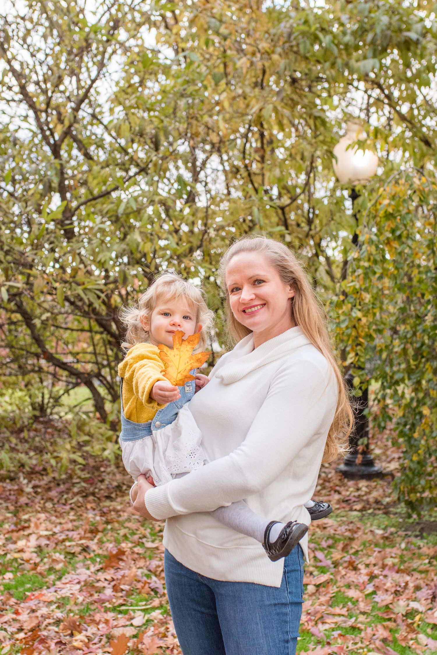young girl proudly holding out a leaf while her mother holds her during a fall family portrait session in the DC area