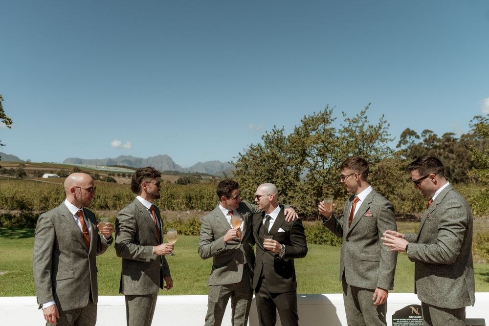 A group of men in gray suits stand together on a patio overlooking a scenic mountain landscape.