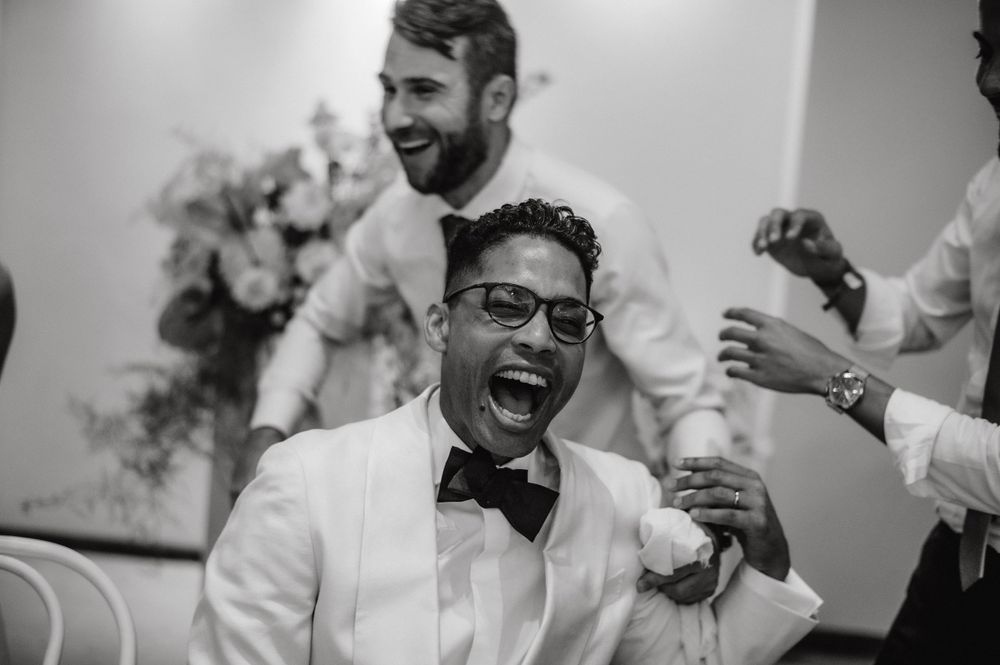 Joyful celebration at a wedding reception with people in formal attire laughing and smiling.