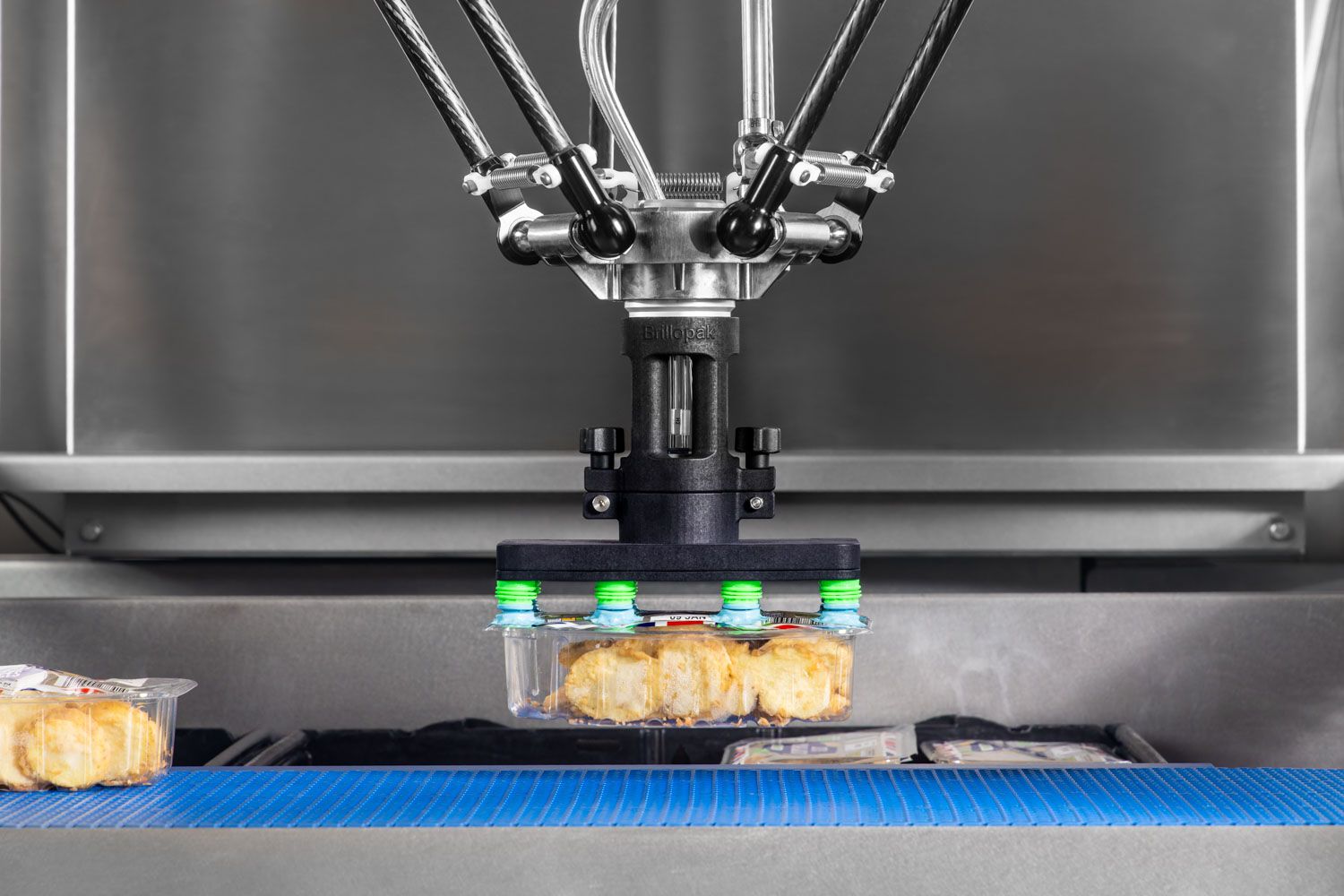 Industrial delta robot arm picking packaged baked goods on a conveyor belt in automated food processing factory