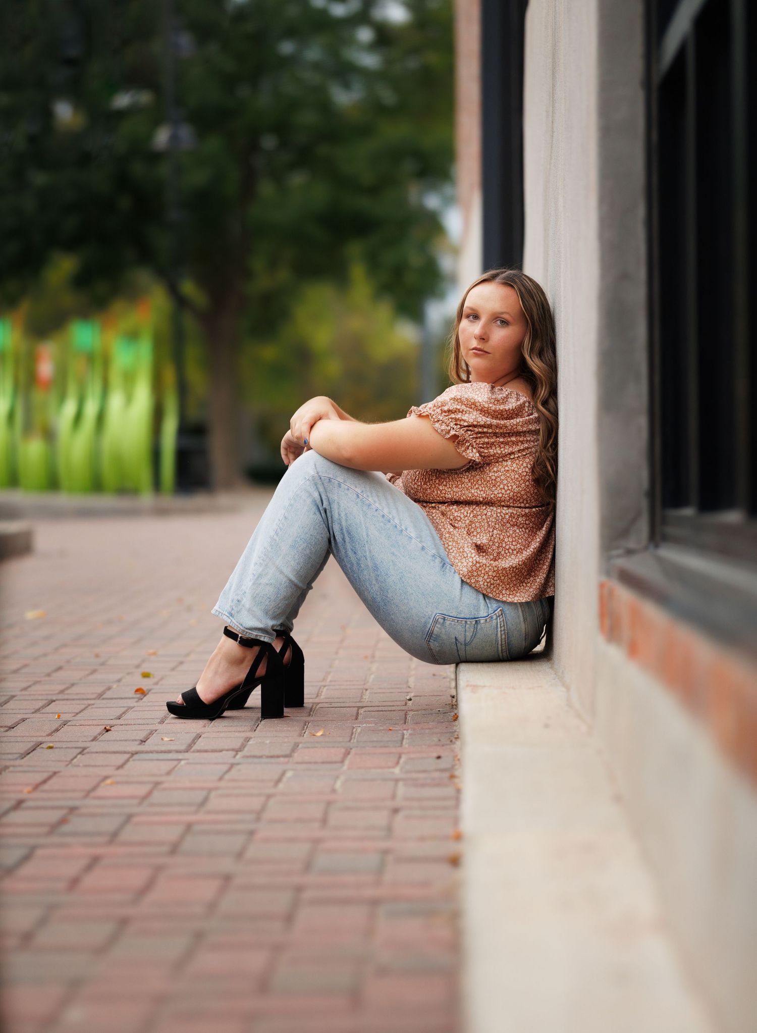 Fashion portrait of woman in jeans and sequin top sitting against building wall.