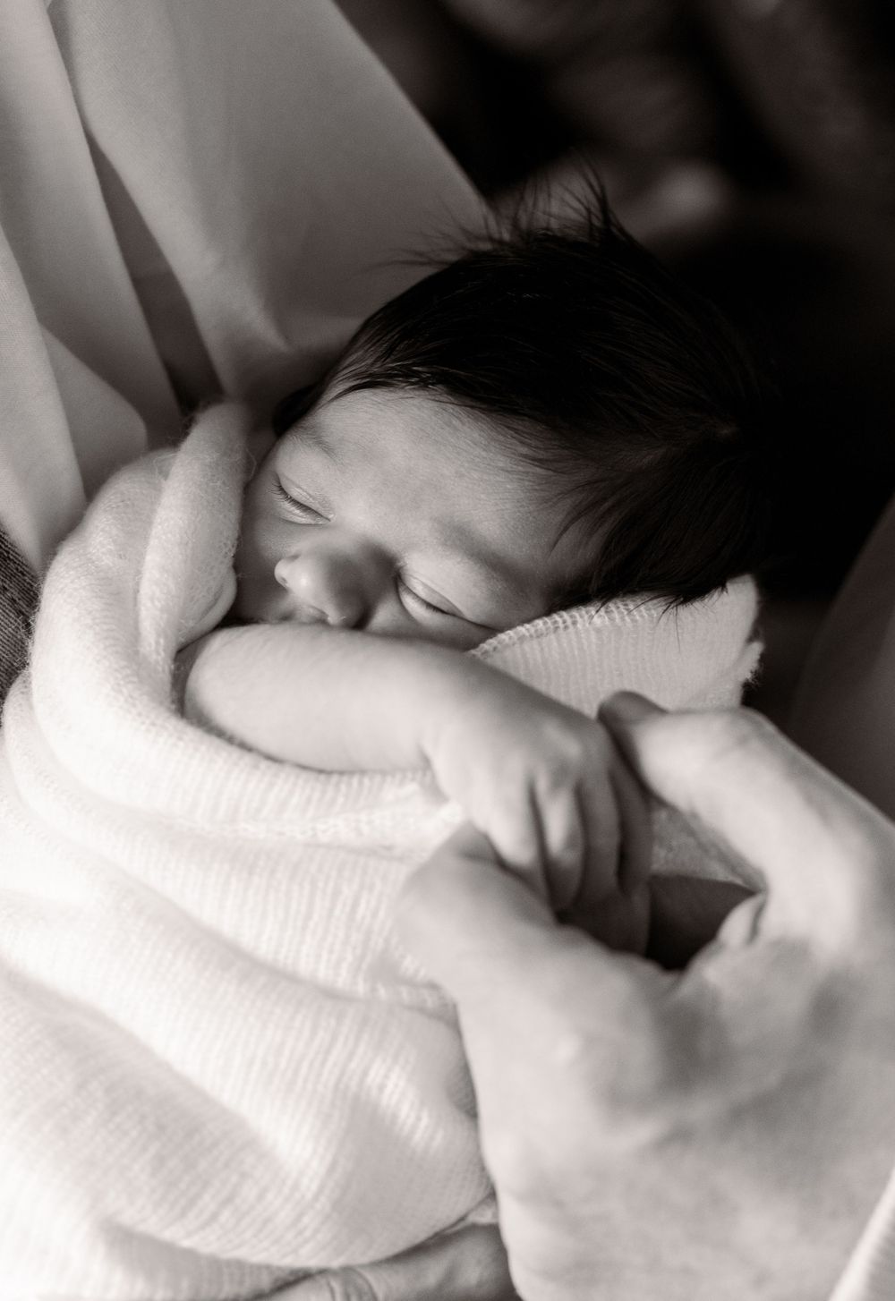 A sleeping newborn swaddled in white fabric captured in black and white photography.