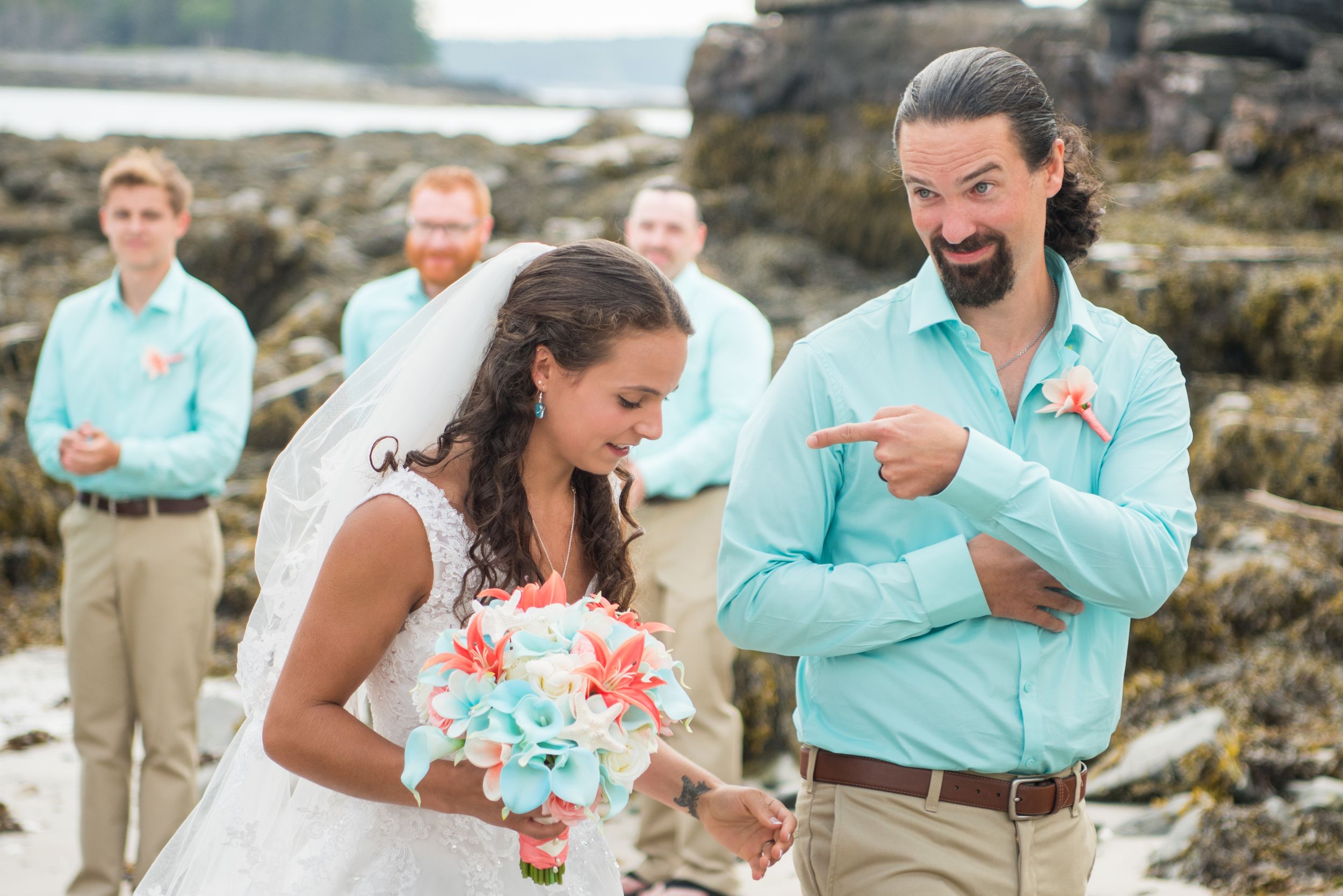A couple shares an emotional moment during their beachside wedding ceremony with teal and coral accents.