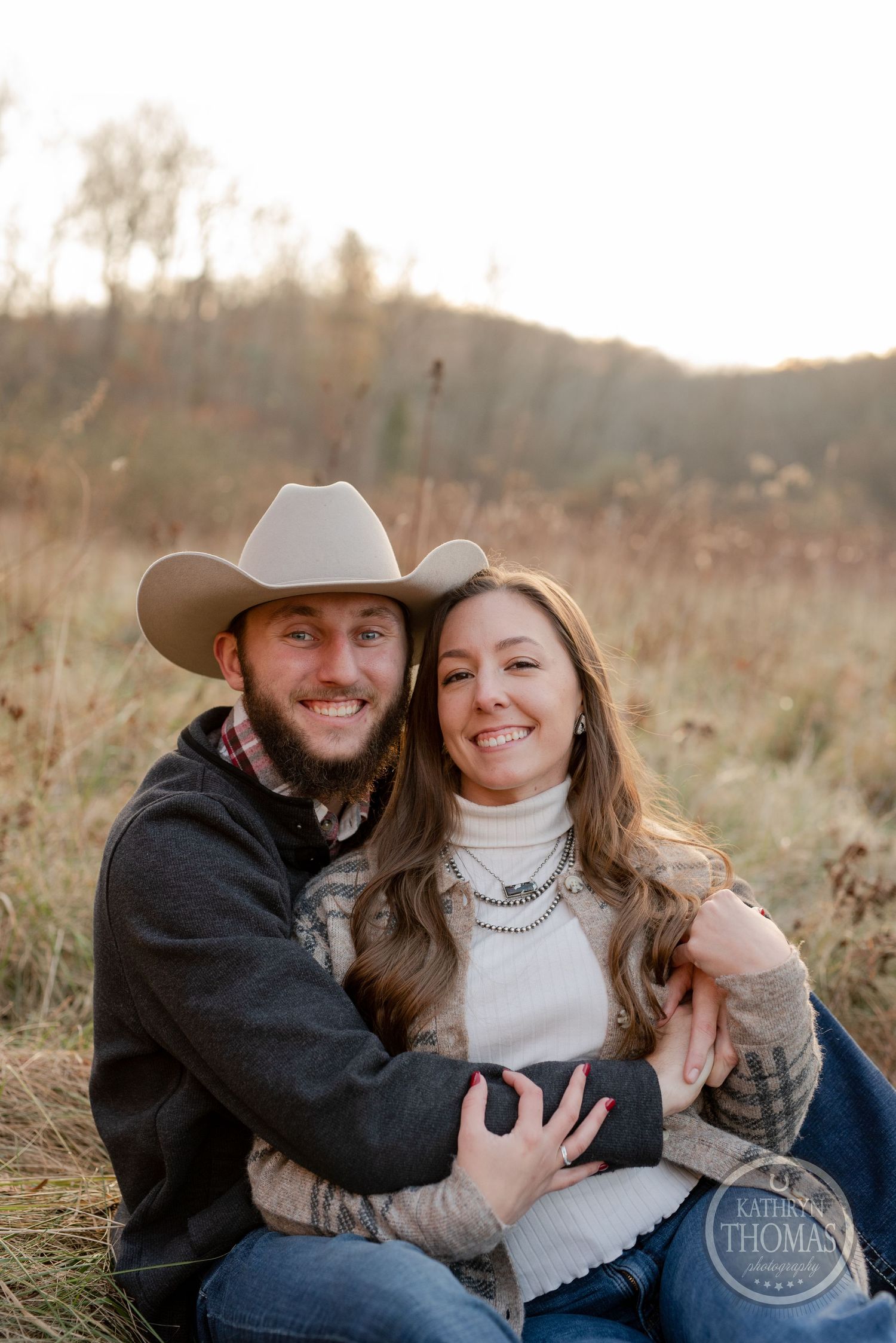 A cozy autumn engagement photo shows a couple embracing in warm evening light.