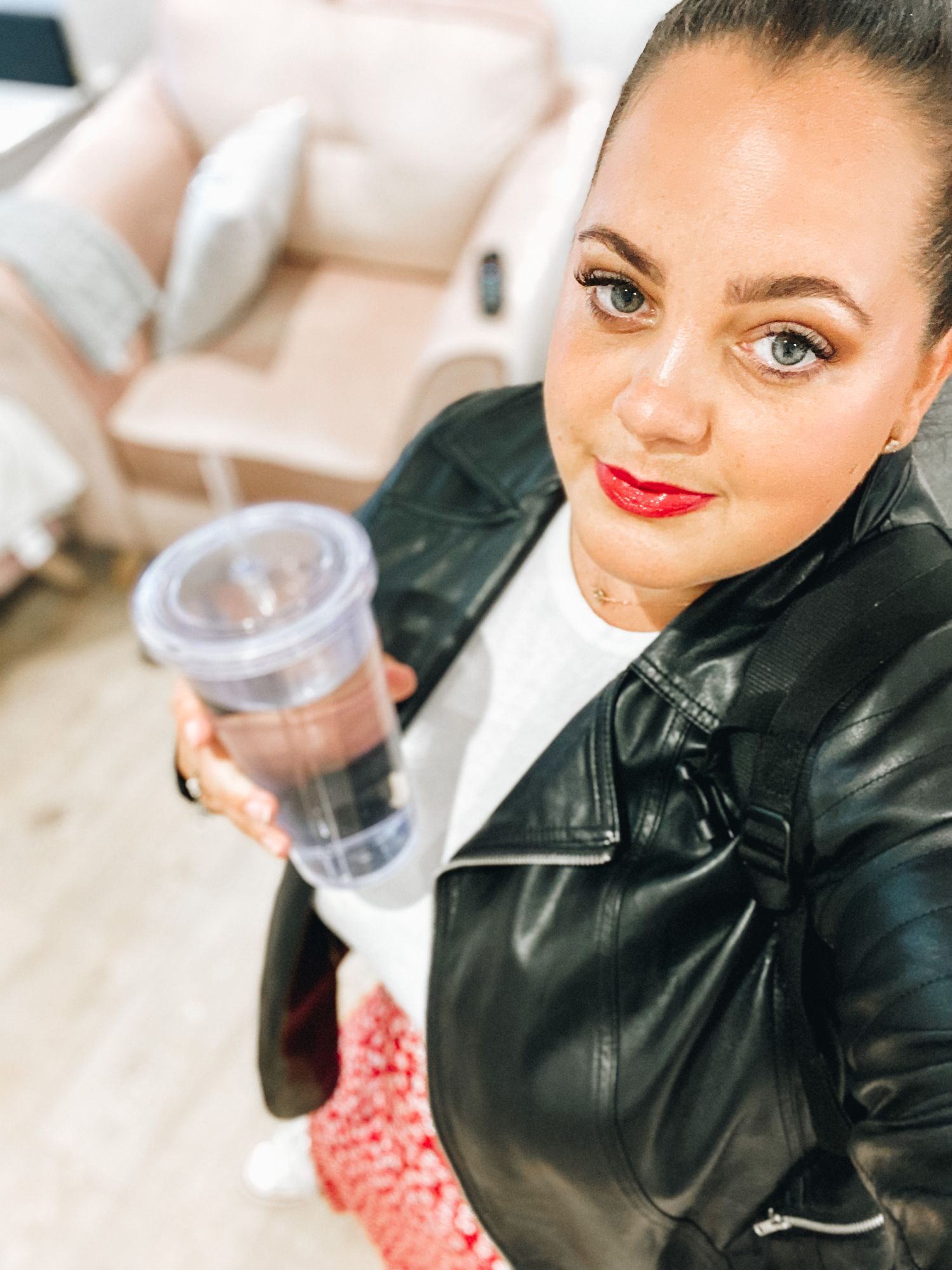 Close up of woman in leather jacket holding beverage against white background.