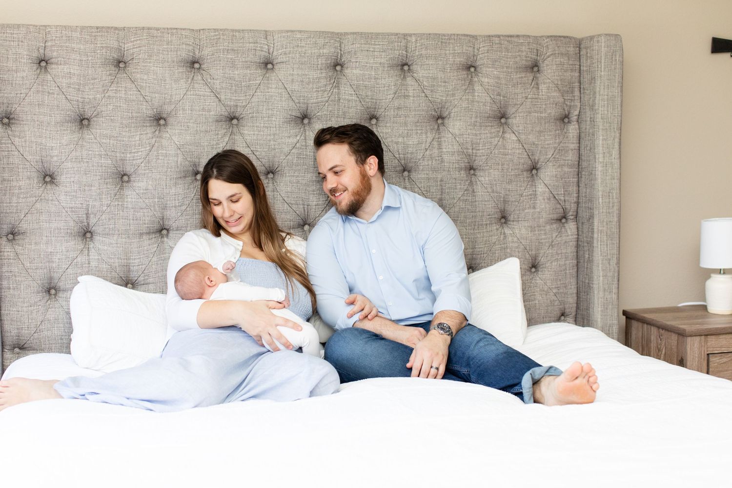 Family relaxing together on bed with tufted gray headboard.