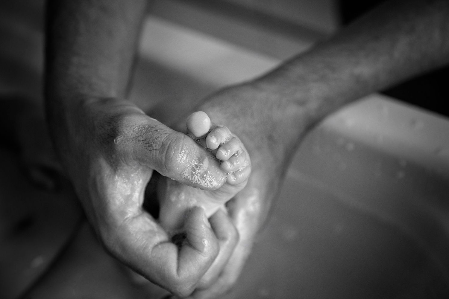 A tender black and white portrait of a parent holding a baby's tiny foot.