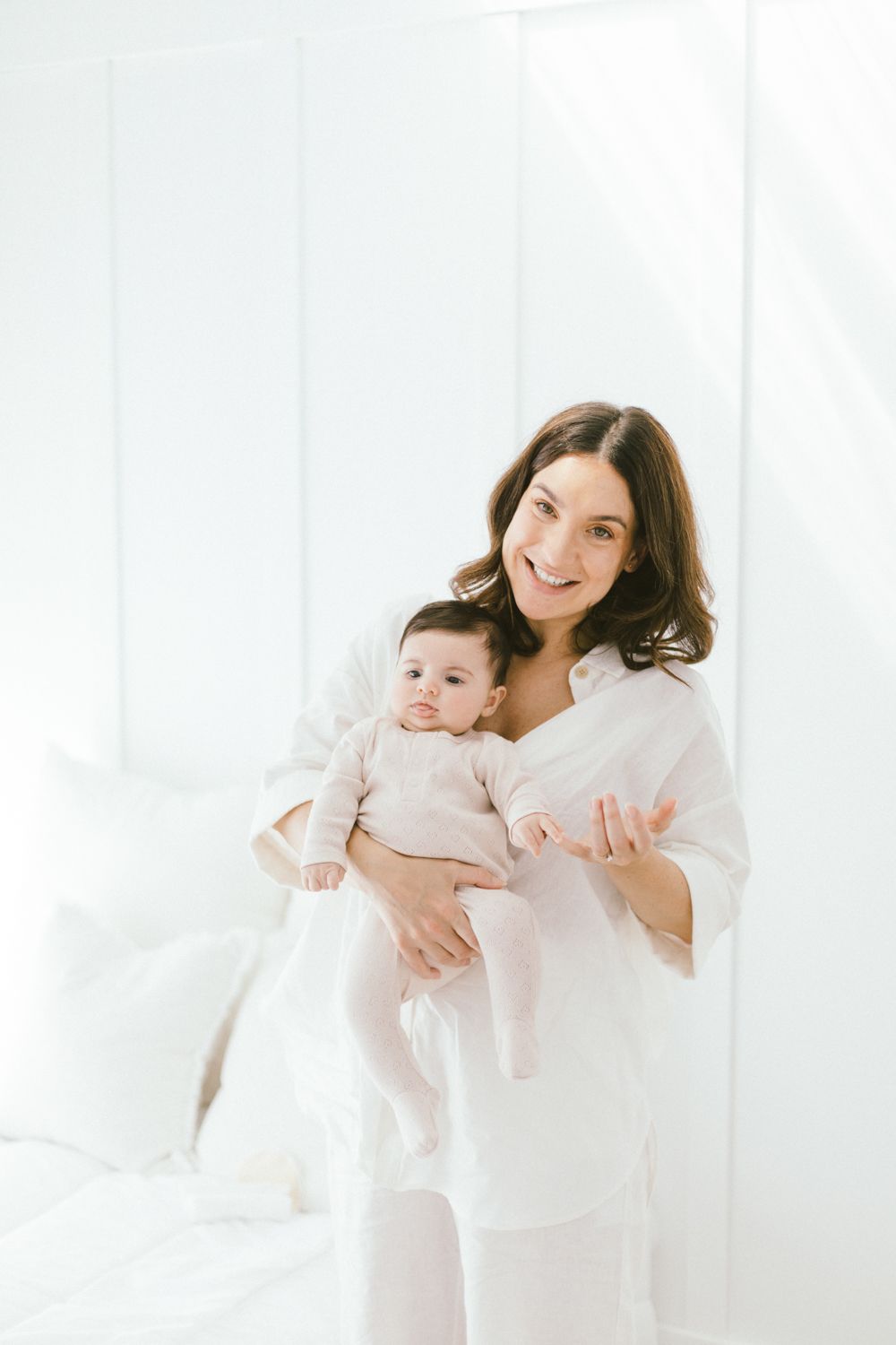 Bright lifestyle portrait of caregiver holding infant against white wall.