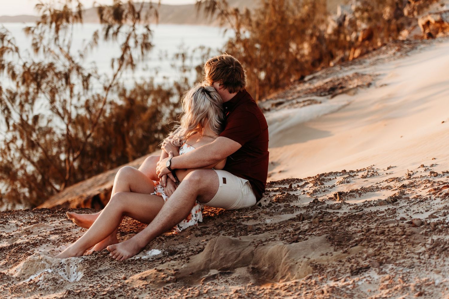 Couple sitting together on coastal cliff during golden hour sunset.