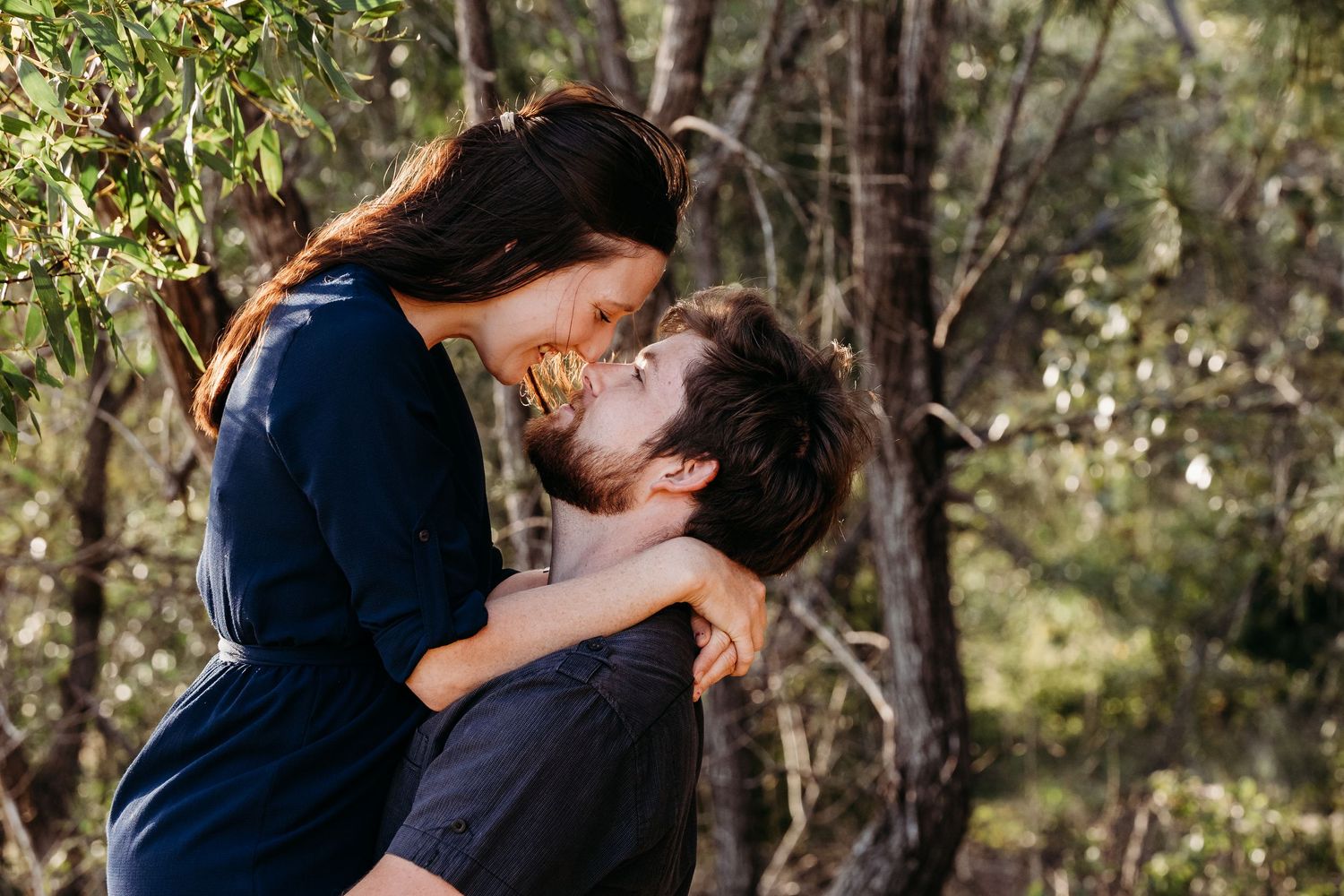 A couple sharing a joyful embrace in a wooded forest setting.