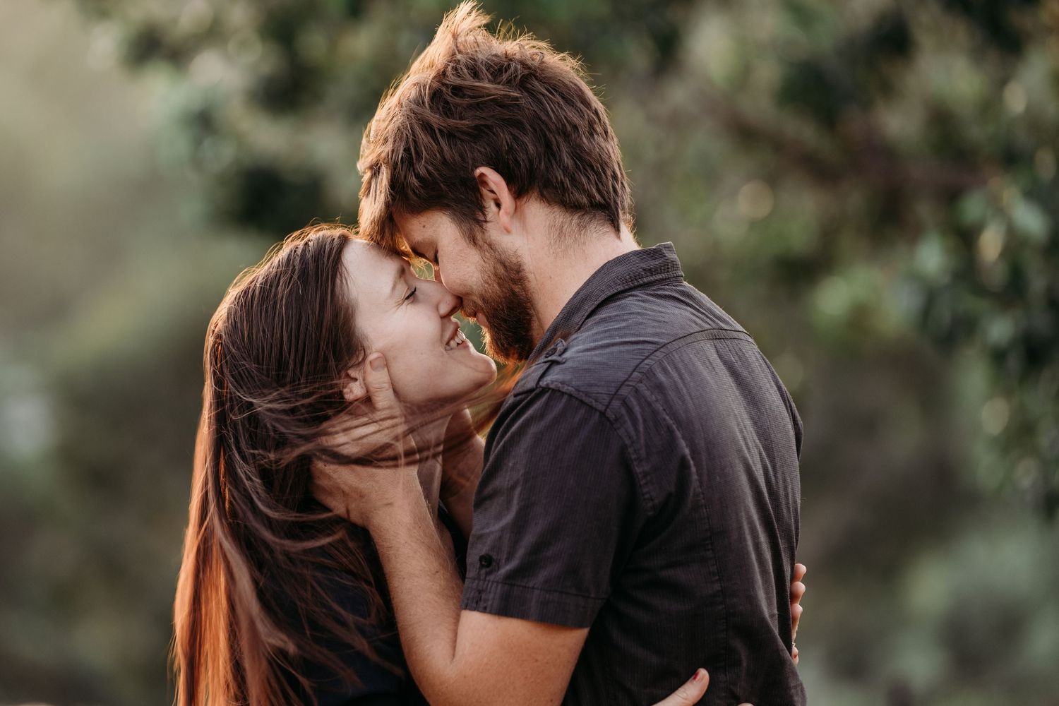 A romantic couple sharing an intimate moment together against a blurred natural background.
