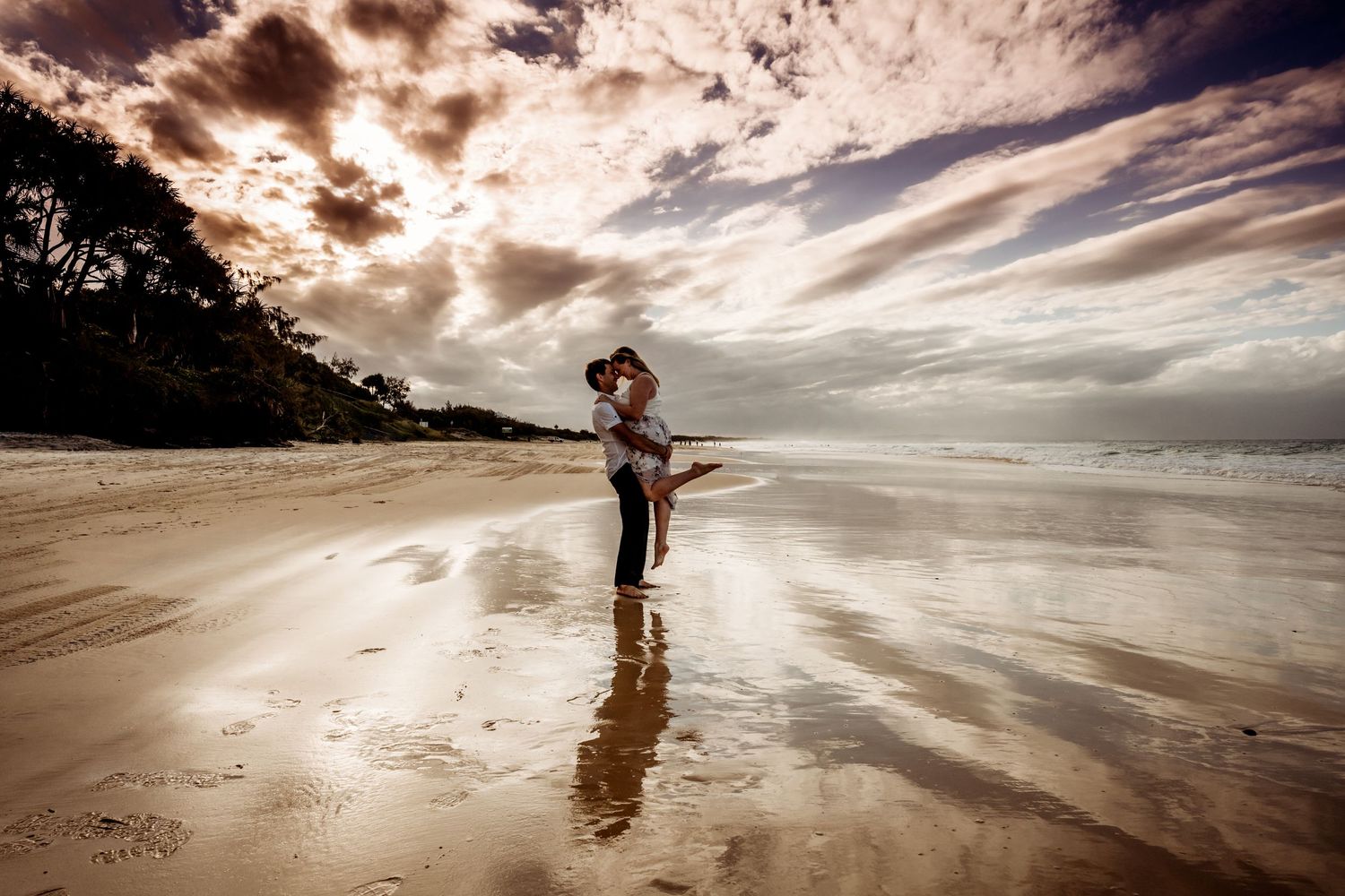 A silhouetted figure stands on a beach with dramatic cloudy sunset sky.