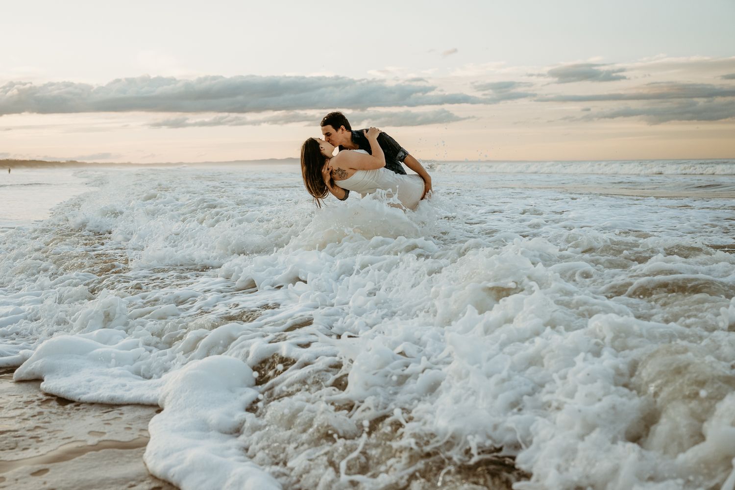 Couple sharing an intimate moment in crashing ocean waves at sunset.