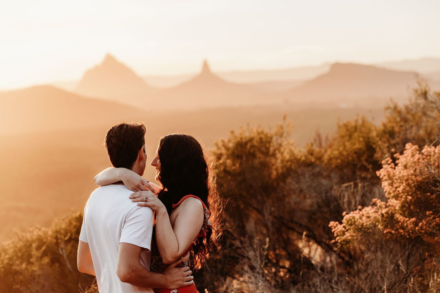Two figures embrace against a backdrop of misty mountain peaks at sunset.