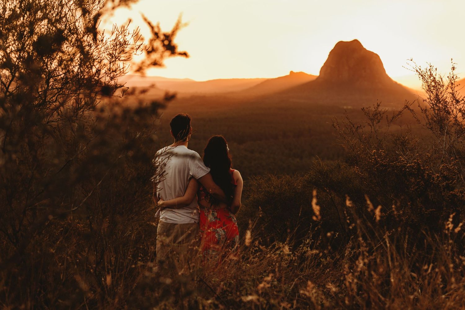 Couple watching sunset over dramatic mountain landscape from scenic viewpoint.