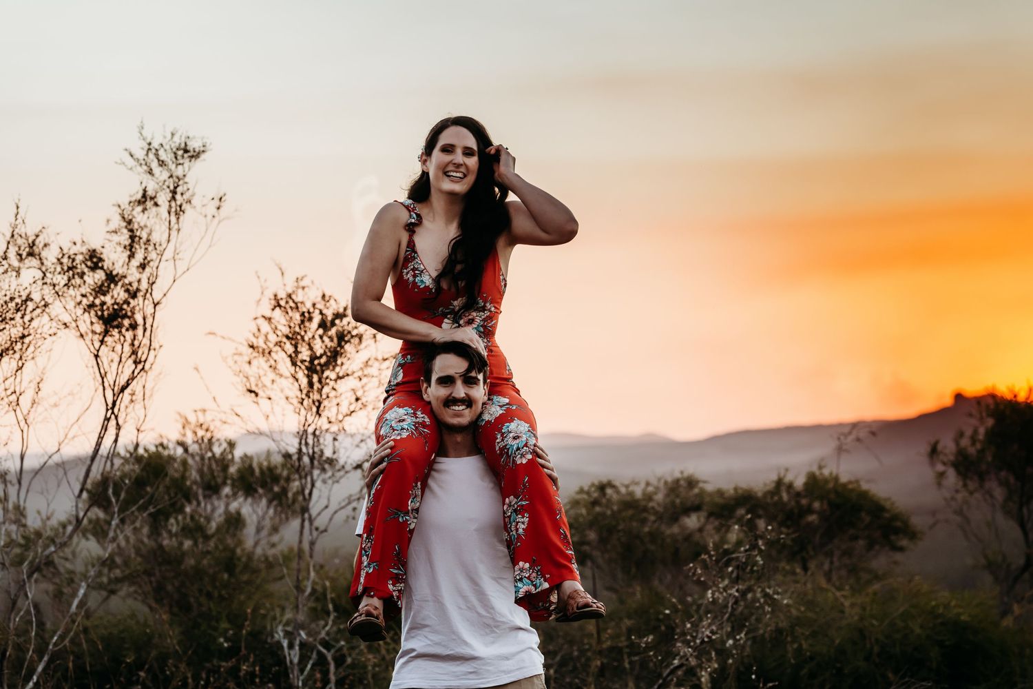 A playful couple enjoys a piggyback ride during sunset in nature.