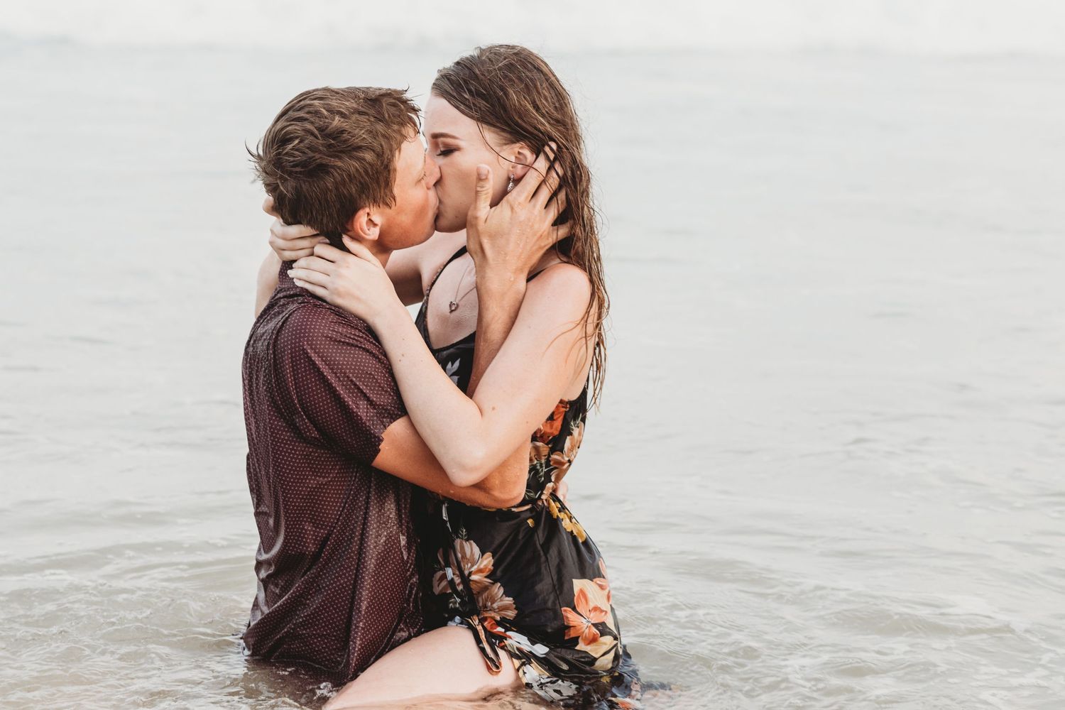Romantic beach embrace with waves and overcast sky in background.