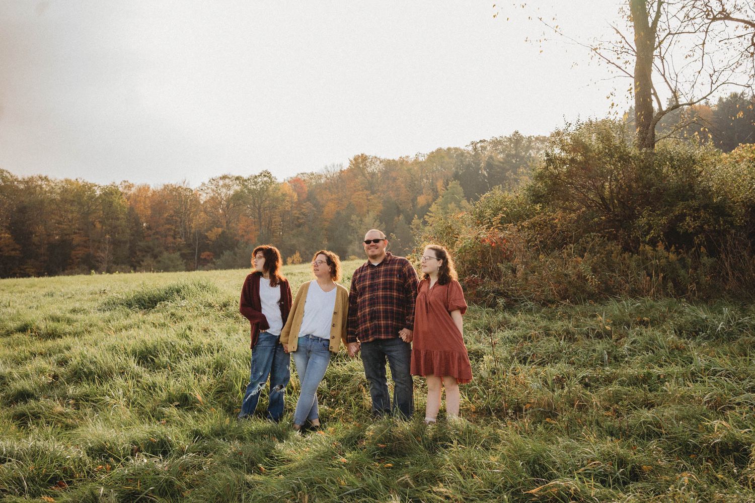 Group walking together in sunny autumn field with fall foliage in background.