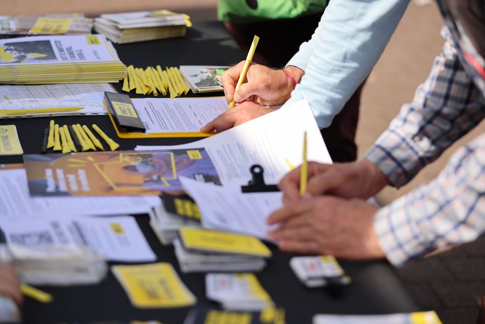 People signing documents at a table covered with papers and sticky notes.