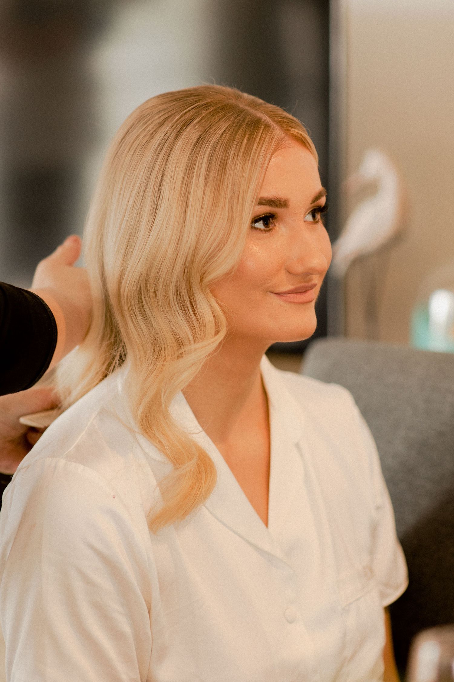 Someone gets their hair styled while wearing a white robe in warm lighting.