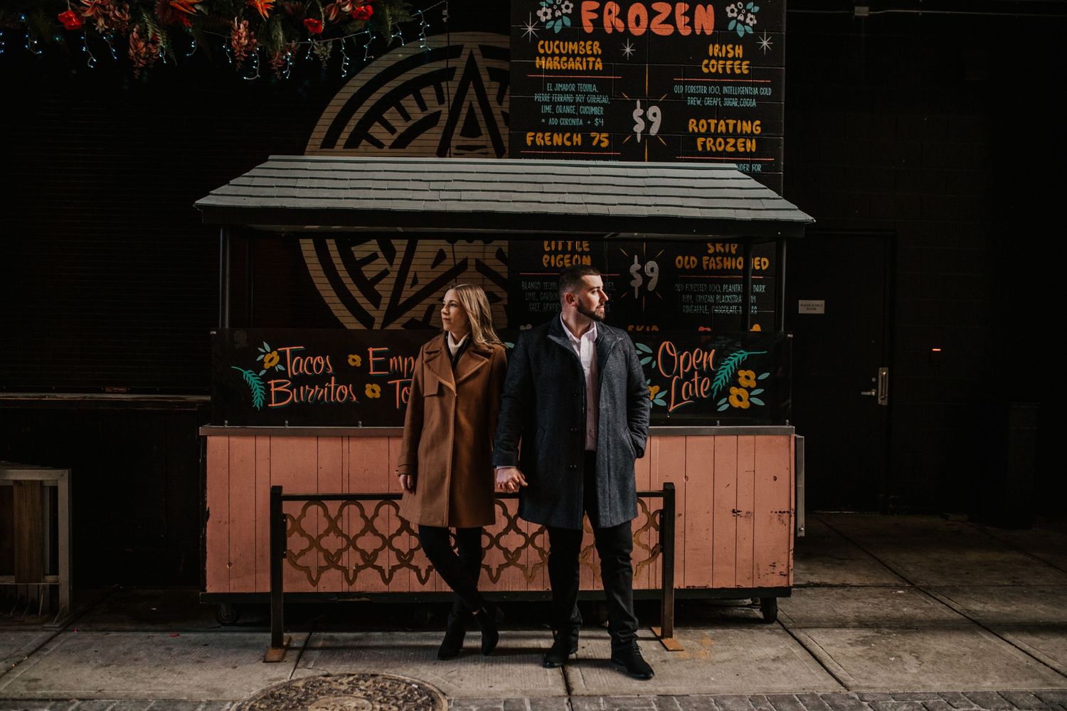 Two people stand together in front of a frozen drink stand at night.