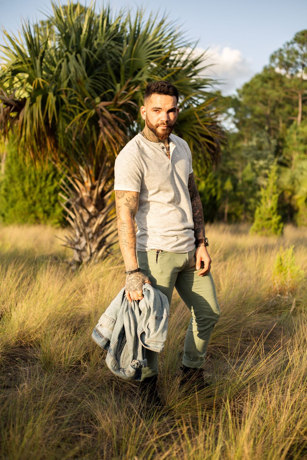 Person wearing polo shirt and khakis stands in grassy area with tropical plants.