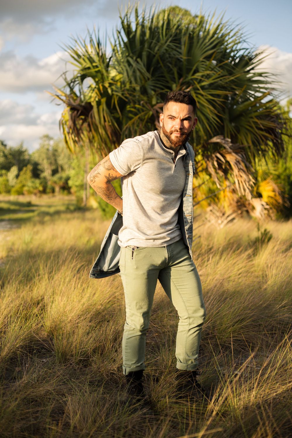Person posing in casual outfit against palm trees during sunset.