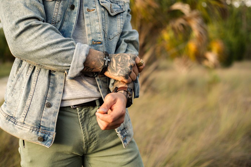 Close up of tattooed hands adjusting a denim jacket sleeve.