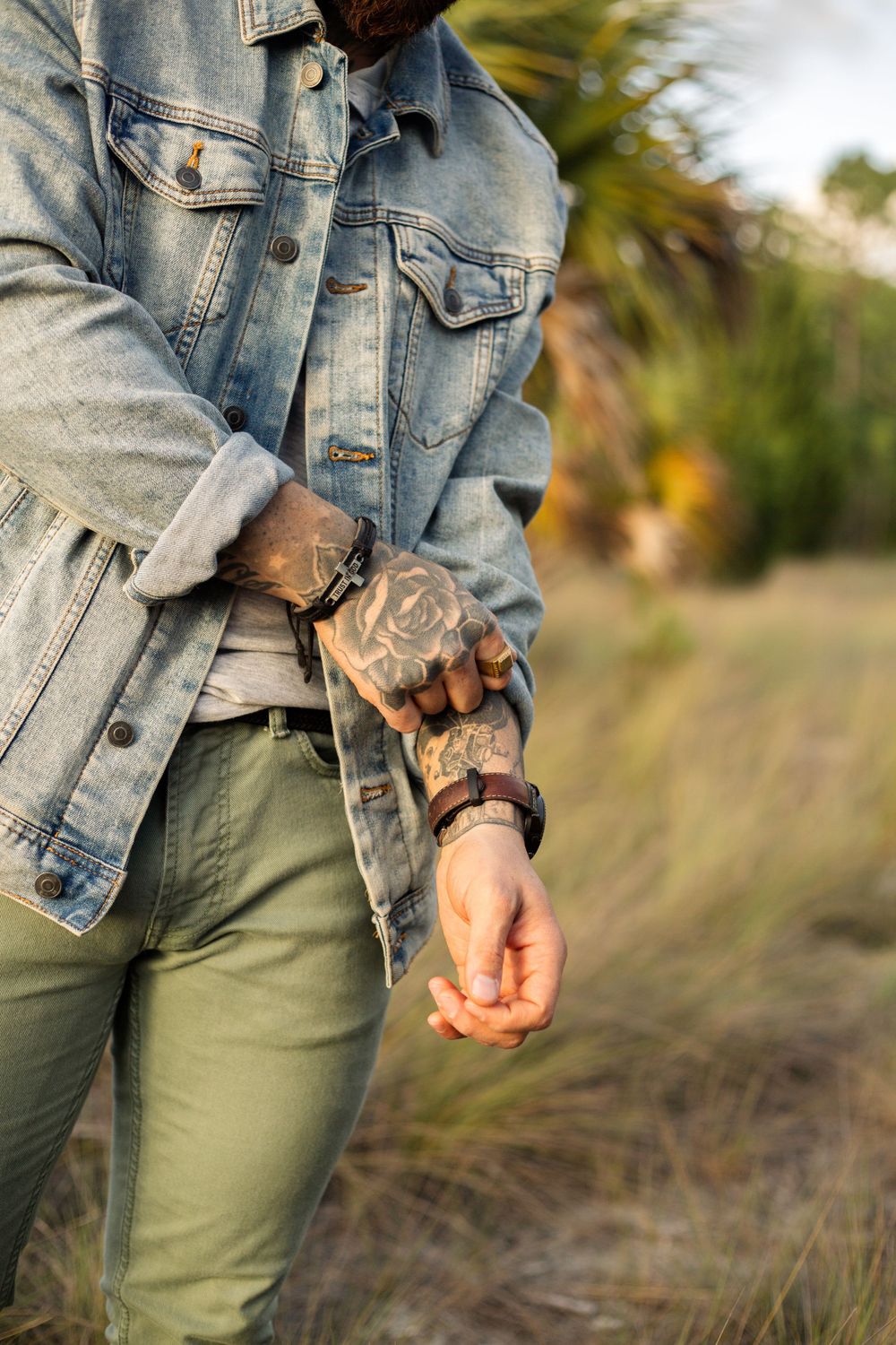 Detailed view of tattooed arms and wrists with denim jacket and olive pants.