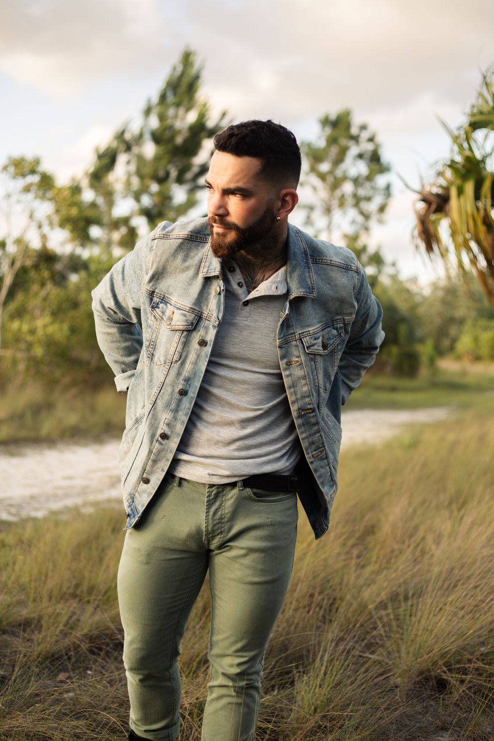 Person in light wash denim jacket and olive pants standing outdoors at sunset.