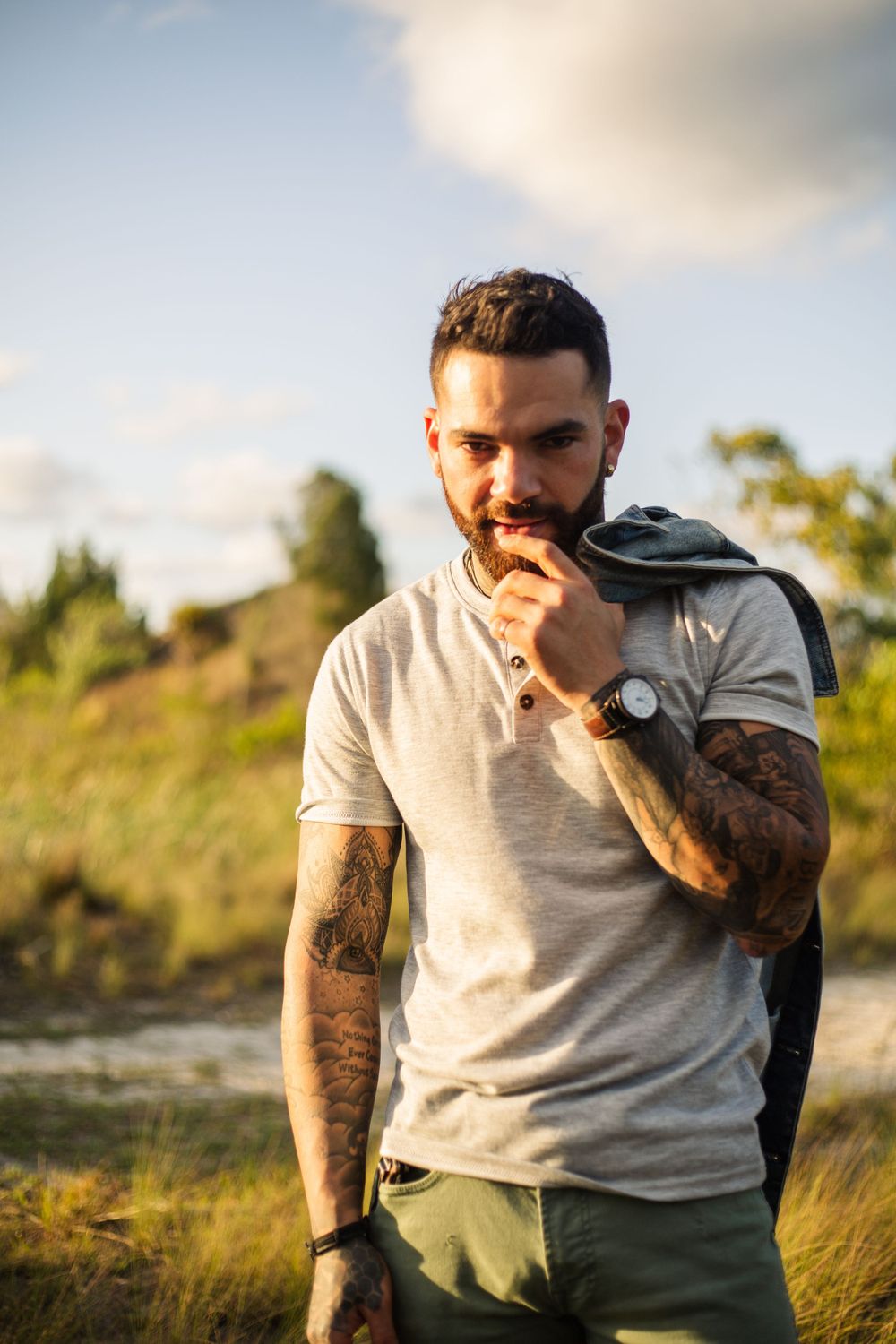 Person in grey t-shirt with tattoos contemplating in golden hour light.