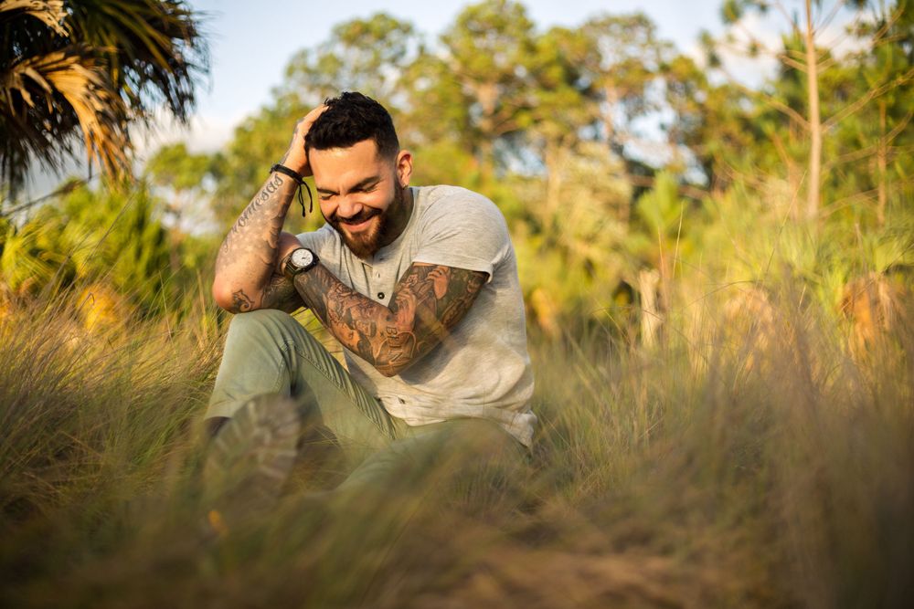 A person smiles while sitting in tall grass during golden hour.