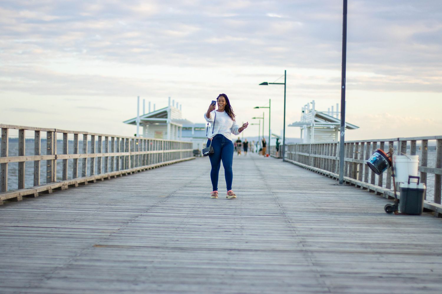 Person walking on wooden pier during cloudy day with boats in background.