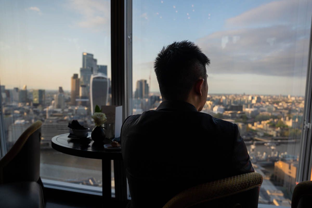 Silhouette of person looking out window at city skyline during sunset.