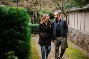 Couple walking along garden path surrounded by greenery and traditional stone walls.